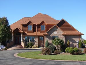 Large, upscale brick home with gables, roof peaks and valleys topped with rust-colored steel shingles