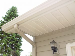 Off-white guttering and soffit that looks like roof trim on a house with tan lap siding and an ornamental mounted lamp