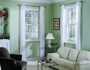 Corner of a furnished living room with green walls that have a double-hung white-frame window on each wall