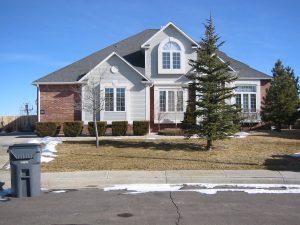Upscale two-story home with light gray lap siding and patches of snow in the yard and street in front 