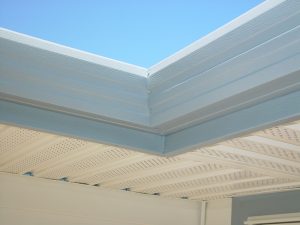 Gray designer-style gutters above beige soffit and and siding in detail shot of the exterior corner of a home